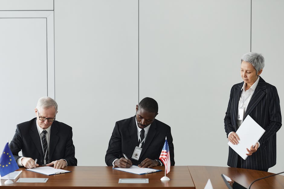 Executives signing international agreement with EU and US flags displayed on a wooden table.